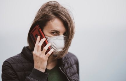 A woman wearing a valved respirator and talking on a cell phone