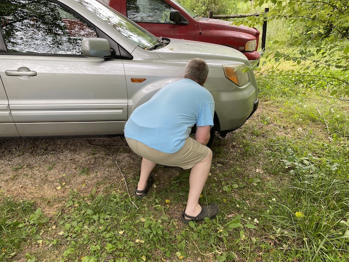 Squatting behind a vehicle's engine block and front passenger wheel